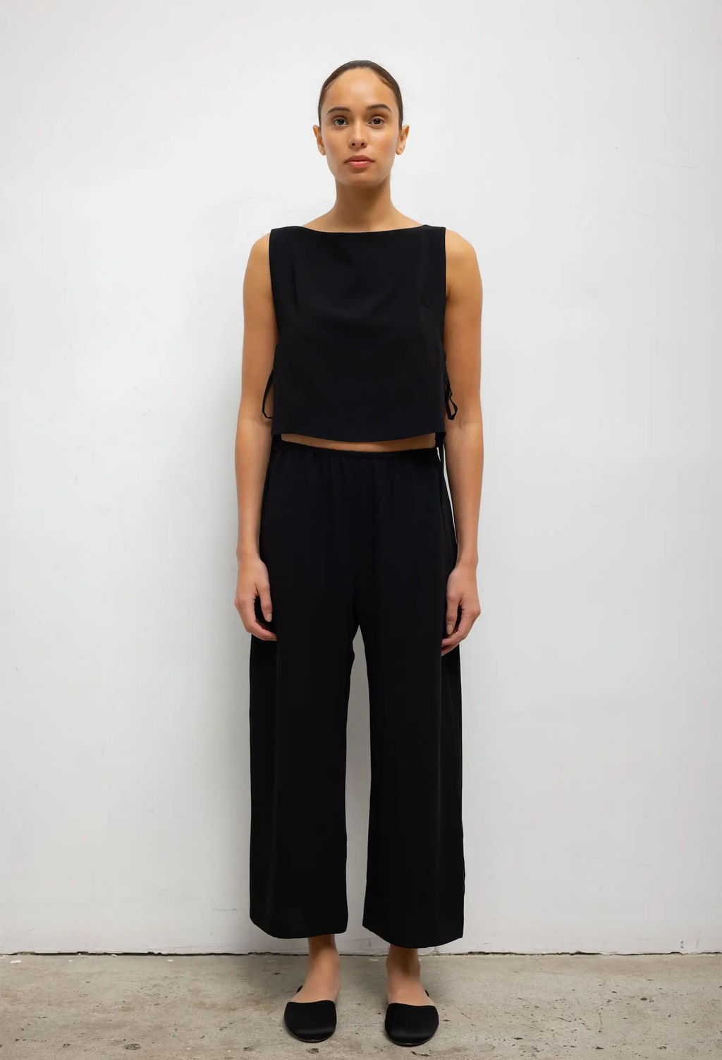 Woman wearing a black sleeveless top and wide-leg pants against a white background