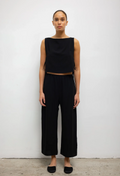 Woman wearing a black sleeveless top and wide-leg pants against a white background