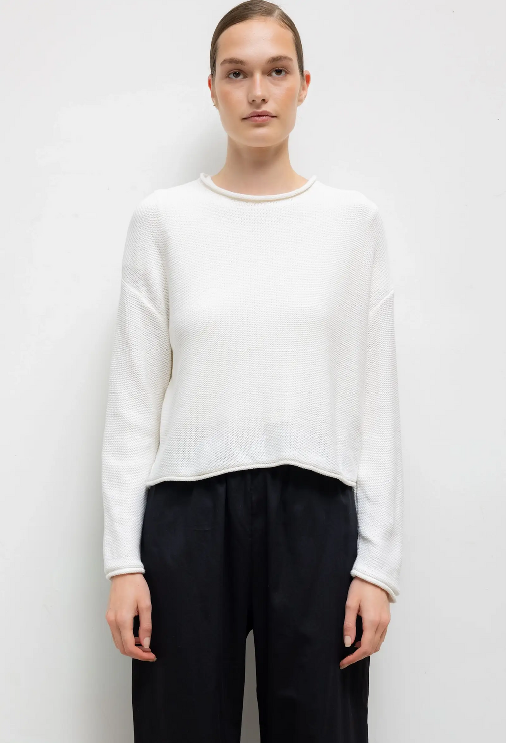 Person wearing a white sweater and black pants on a plain background