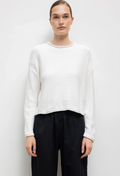 Person wearing a white sweater and black pants on a plain background