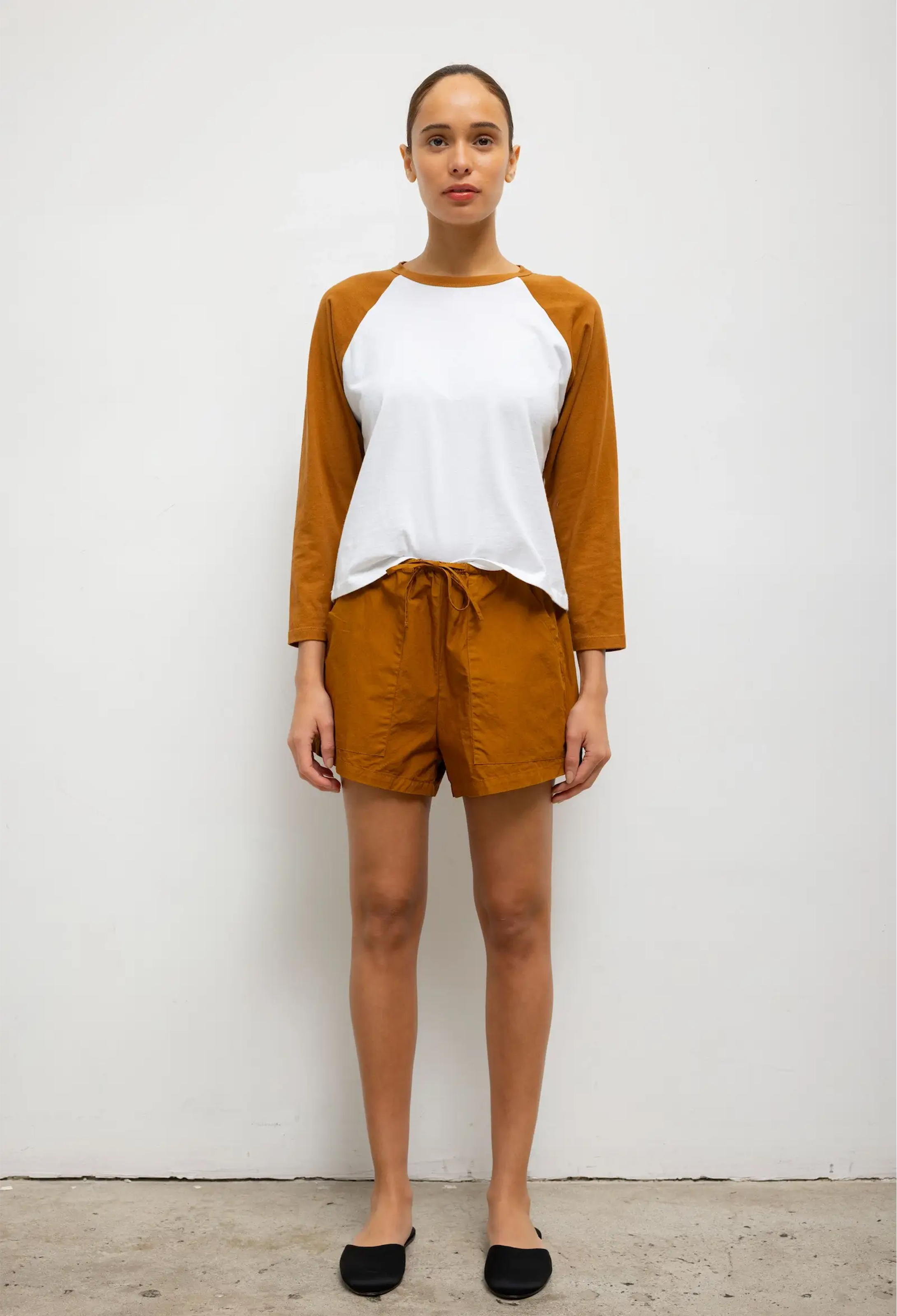 Woman wearing a white top with brown sleeves and rust-colored shorts against a white background
