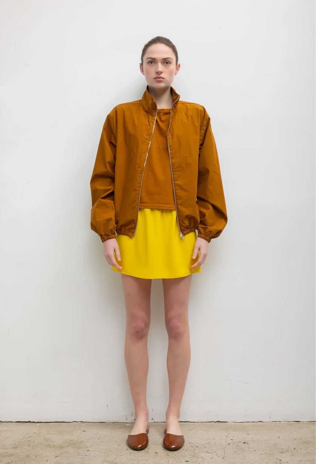 Person wearing a mustard yellow jacket and skirt against a white background