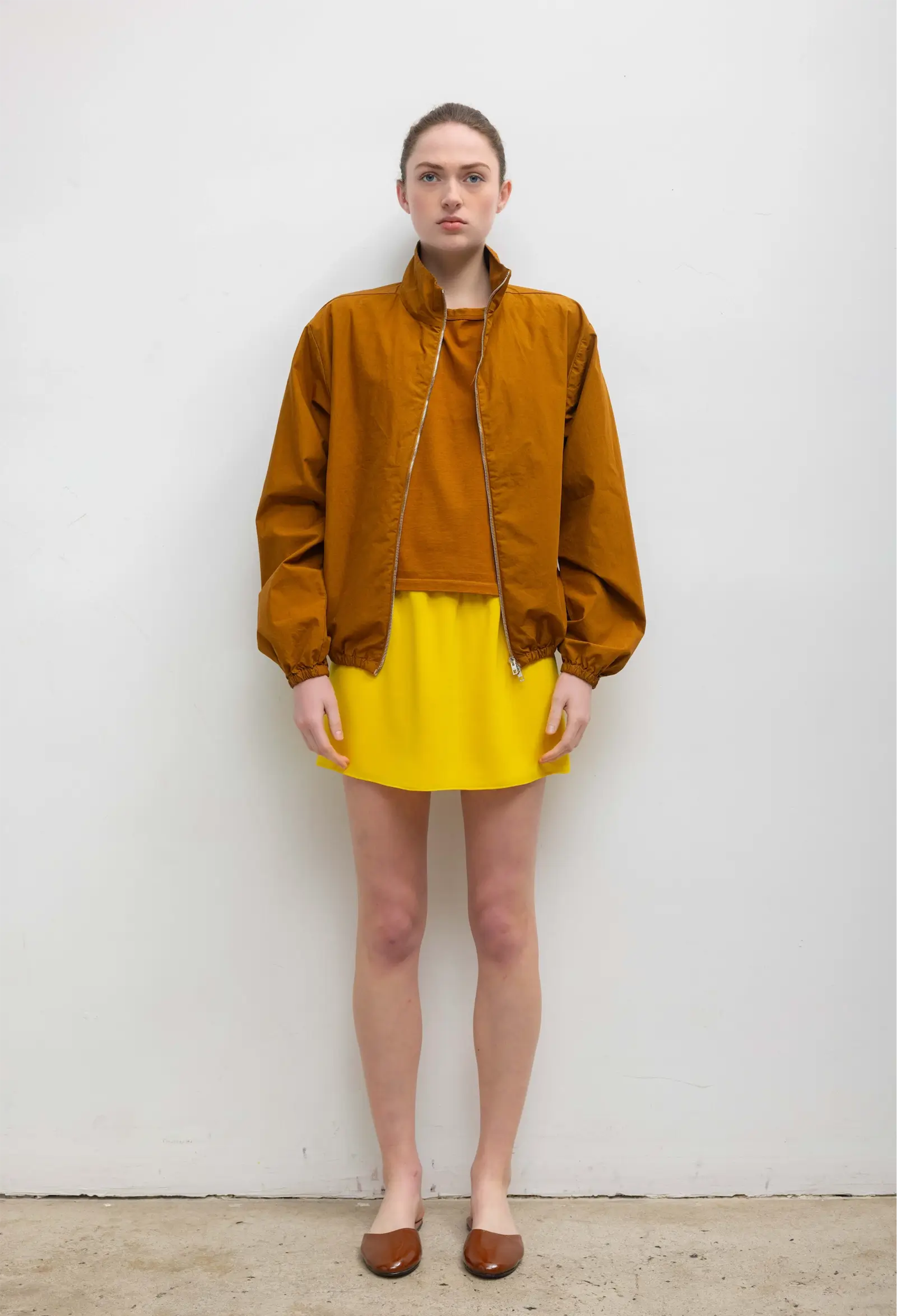 Person wearing a mustard yellow jacket and skirt against a white background