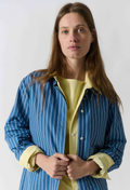 Woman wearing a blue striped shirt over a yellow top against a white background