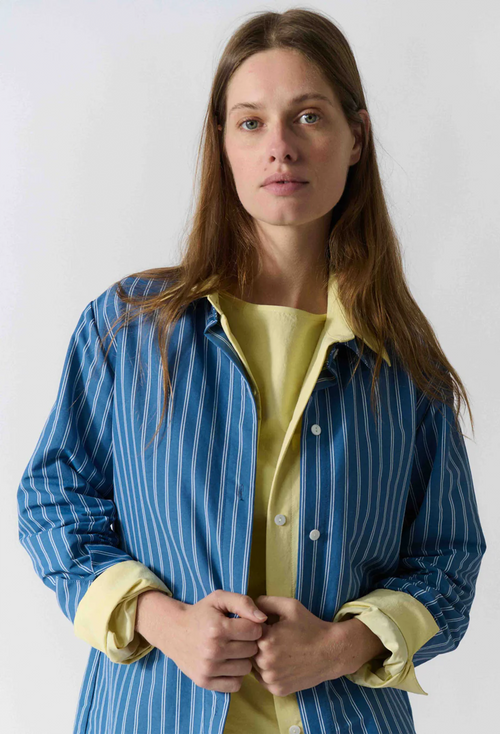 Woman wearing a blue striped shirt over a yellow top against a white background