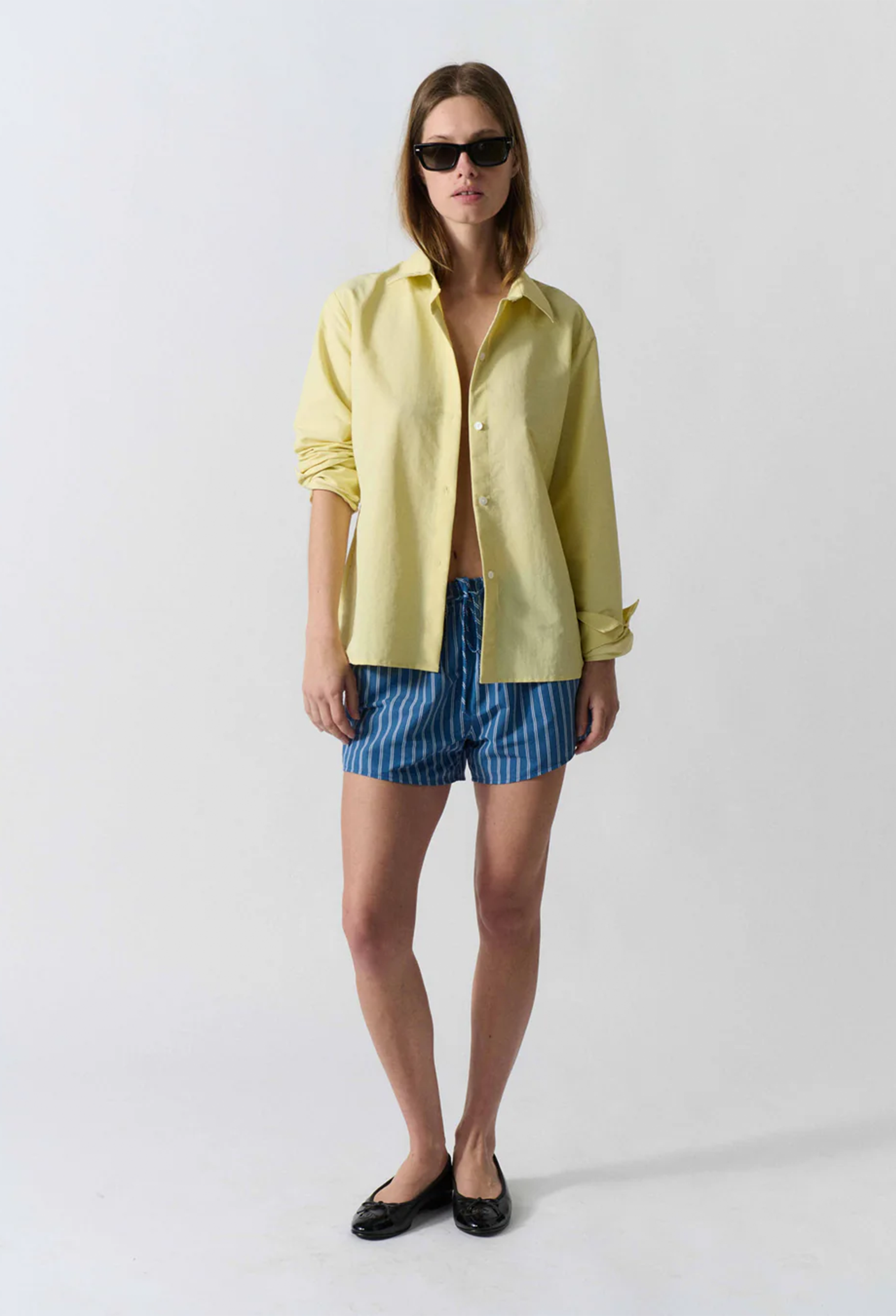 Woman wearing a yellow shirt and blue striped shorts on a white background