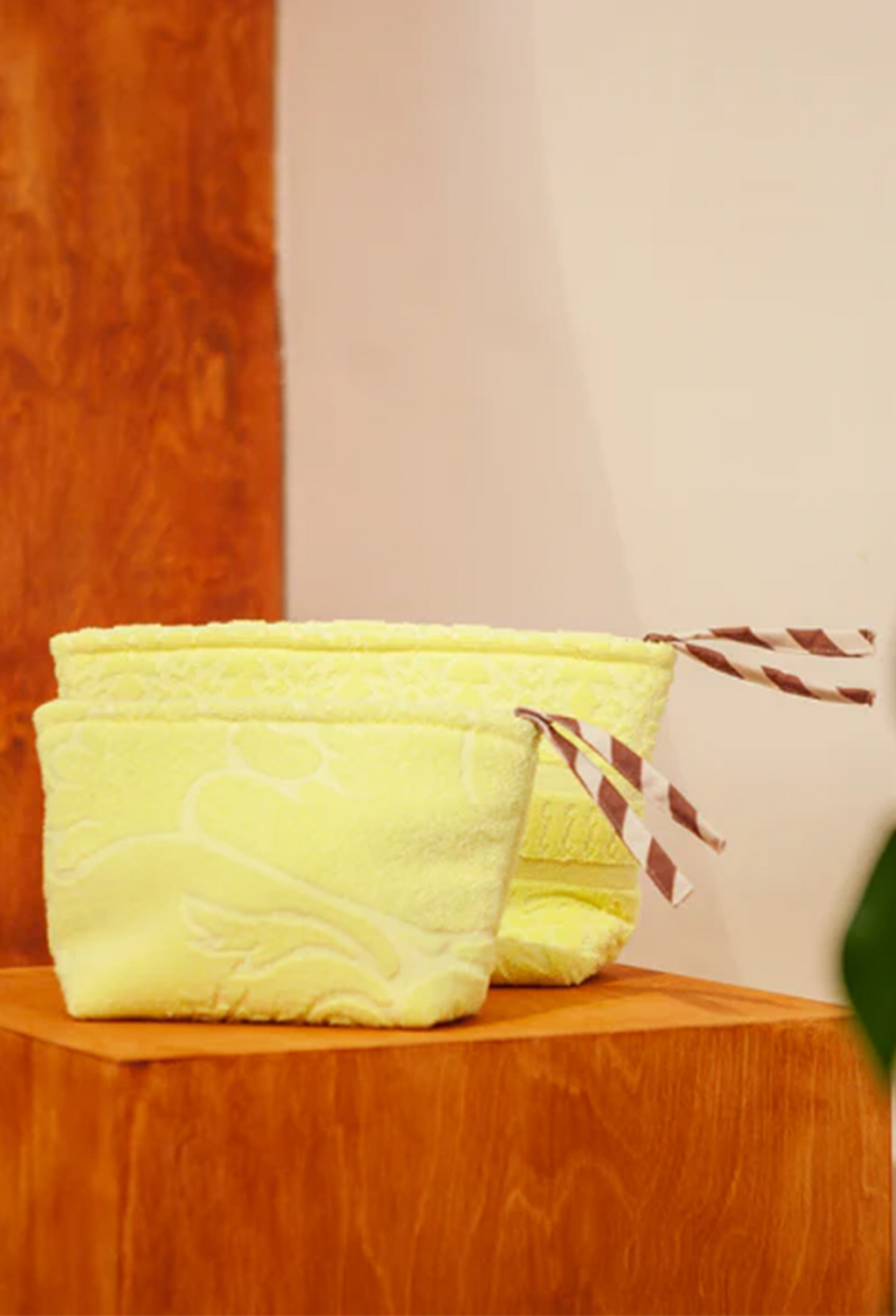 Two pale yellow fabric pouches with floral patterns and brown-and-white striped drawstring ties, displayed on a wooden surface against a cream wall.