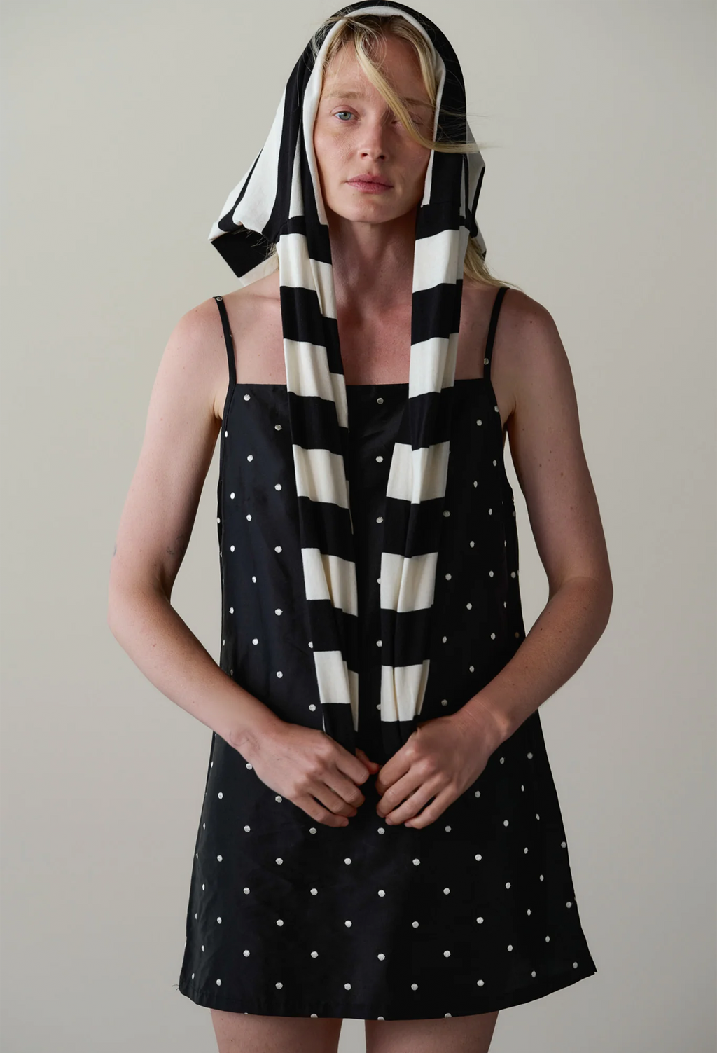 A model wearing a black and white striped and polka dot dress with a matching striped headscarf, standing against a plain light gray background.