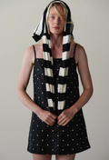 A model wearing a black and white striped and polka dot dress with a matching striped headscarf, standing against a plain light gray background.