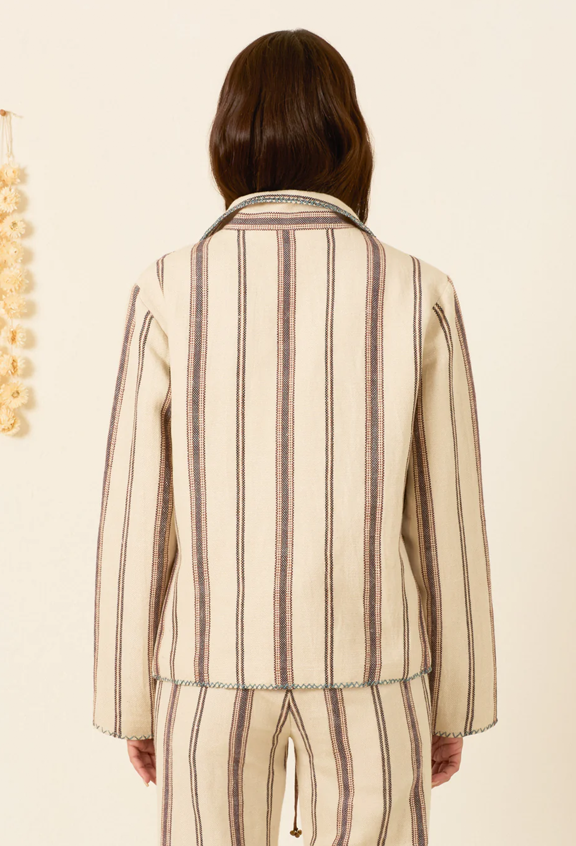 A person shown from the back wearing a cream-colored striped jacket and matching striped pants against a warm off-white background.