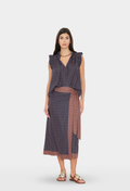 A woman modeling a sleeveless wrap-style midi dress with a navy and rust red geometric pattern, set against a plain light gray studio background.