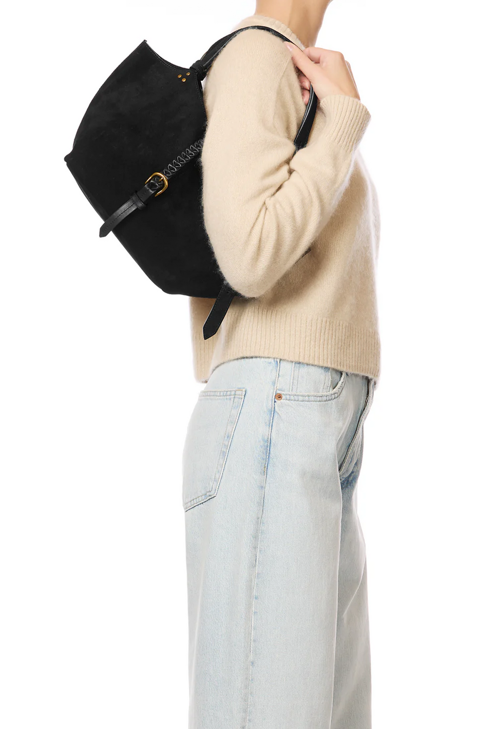A person wearing a beige knit sweater and light blue jeans carries a black shoulder bag with a flap closure and gold-tone hardware against a plain white background.