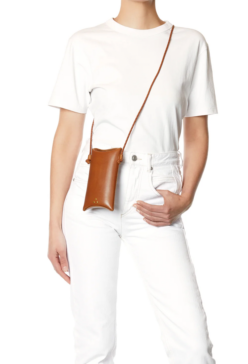 A model wearing a white t-shirt and white jeans, carrying a small brown leather crossbody pouch bag with a matching strap.
