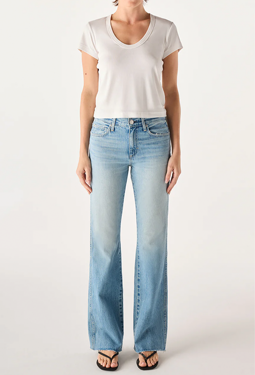 A model wearing a white short-sleeve scoop-neck t-shirt and light-wash blue straight-leg jeans, paired with black flip-flop sandals, against a plain light gray studio background.