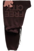 Dark brown sweatpants featuring a large tonal 'FREE CITY' text graphic and a pink dove logo on the upper leg, with an elastic waistband and white drawstring.