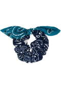 A fabric scrunchie styled as a bow, featuring a navy blue and white paisley pattern on the main body and a solid teal blue patterned bandana on the bow ends, shown against a plain white background.