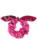 A fabric scrunchie with a bow detail, featuring a vibrant pink and magenta paisley bandana pattern with black accents, isolated on a white background.