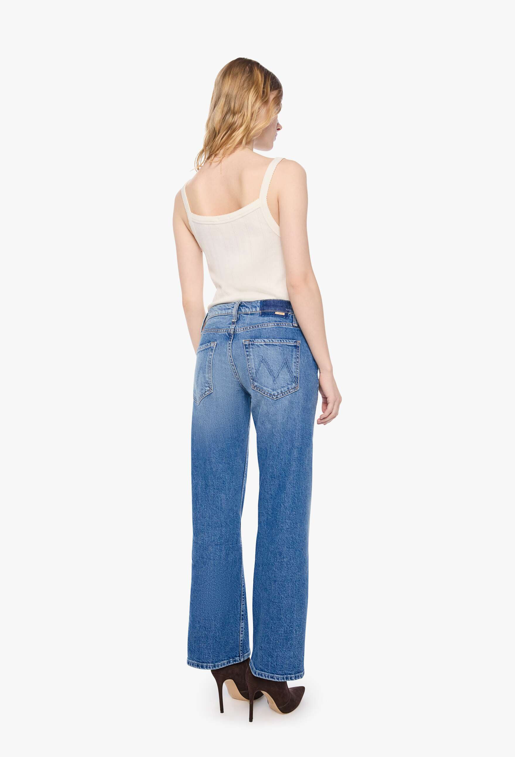 A woman shown from the back wearing blue wide-leg jeans, a cream camisole top, and black high heels against a plain white studio background.