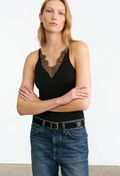 A woman modeling a black ribbed tank top with a lace V-neckline detail, paired with blue jeans and a black belt, against a plain white studio background.