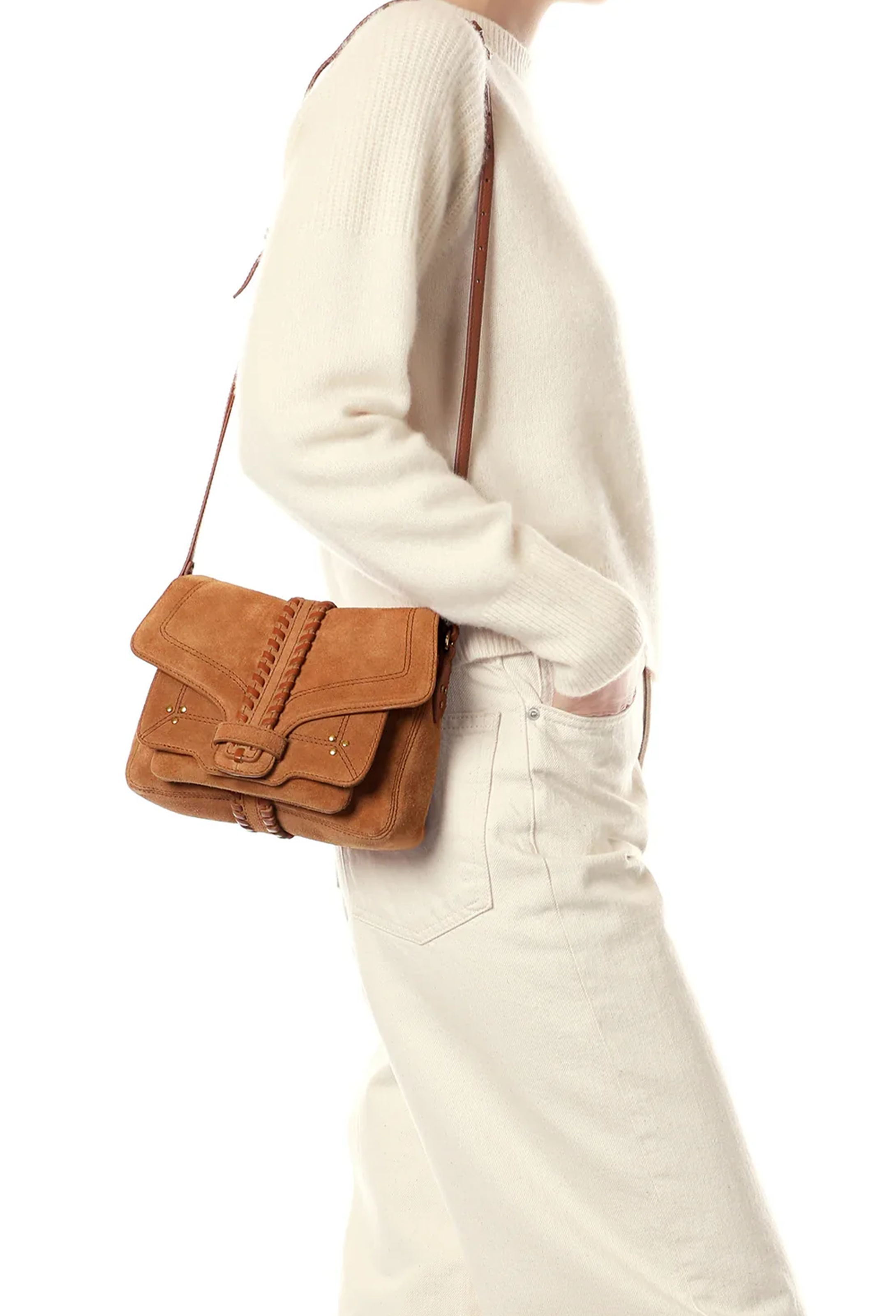 A person wearing a cream ribbed sweater and cream pants carries a brown suede crossbody bag with a matching strap against a plain white background.
