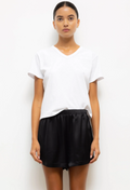 A woman modeling a white short-sleeve V-neck t-shirt and black satin shorts against a plain white background.