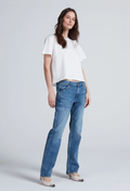 A woman modeling a white short-sleeve crop top and blue straight-leg jeans against a light gray studio background.