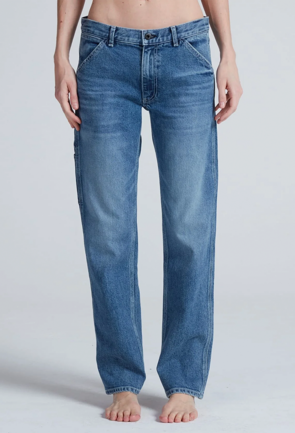 A person wearing straight-leg blue denim jeans, shown from the waist down against a light gray studio background.