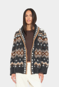 A woman modeling a dark gray open-front knit cardigan with a brown and white Fair Isle pattern and tan trim, worn over a brown top and cream pants against a light gray background.
