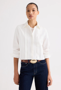 A model wearing a white long-sleeve pleated blouse tucked into dark blue jeans with a brown belt, photographed against a clean white studio background.