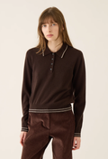A model wearing a dark brown long-sleeve knit polo shirt with contrasting white piping on the collar and hem, paired with matching brown corduroy trousers, against a plain off-white studio background.