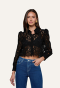 A woman modeling a black lace long-sleeve cropped blouse with puffed shoulders, paired with blue jeans, against a plain off-white studio background.