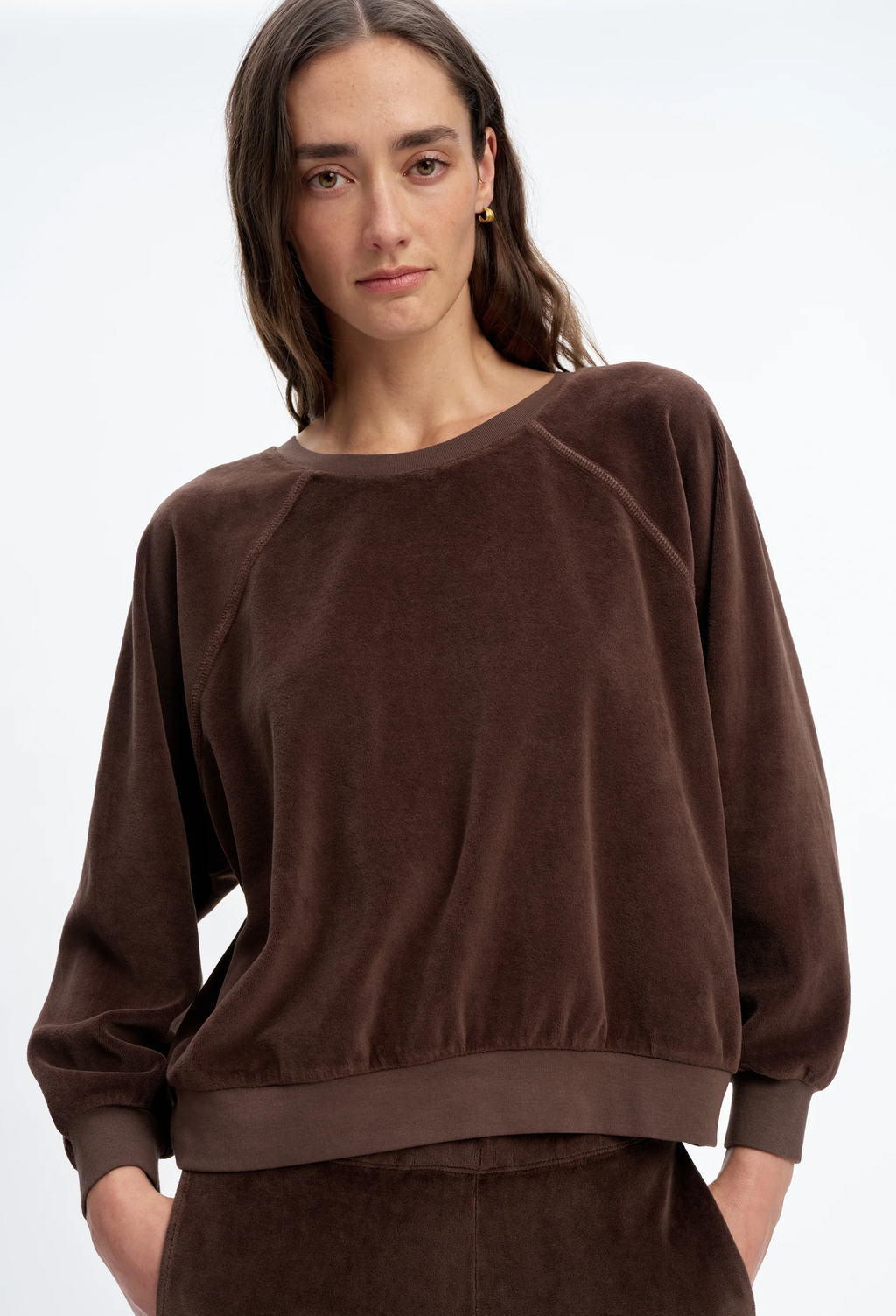 A woman wearing a dark brown velvet long-sleeve sweatshirt and matching pants against a plain white studio background.