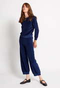 A woman modeling a matching navy blue velour lounge set consisting of a long-sleeve top and wide-leg cropped pants, paired with black Mary Jane shoes against a plain white studio background.