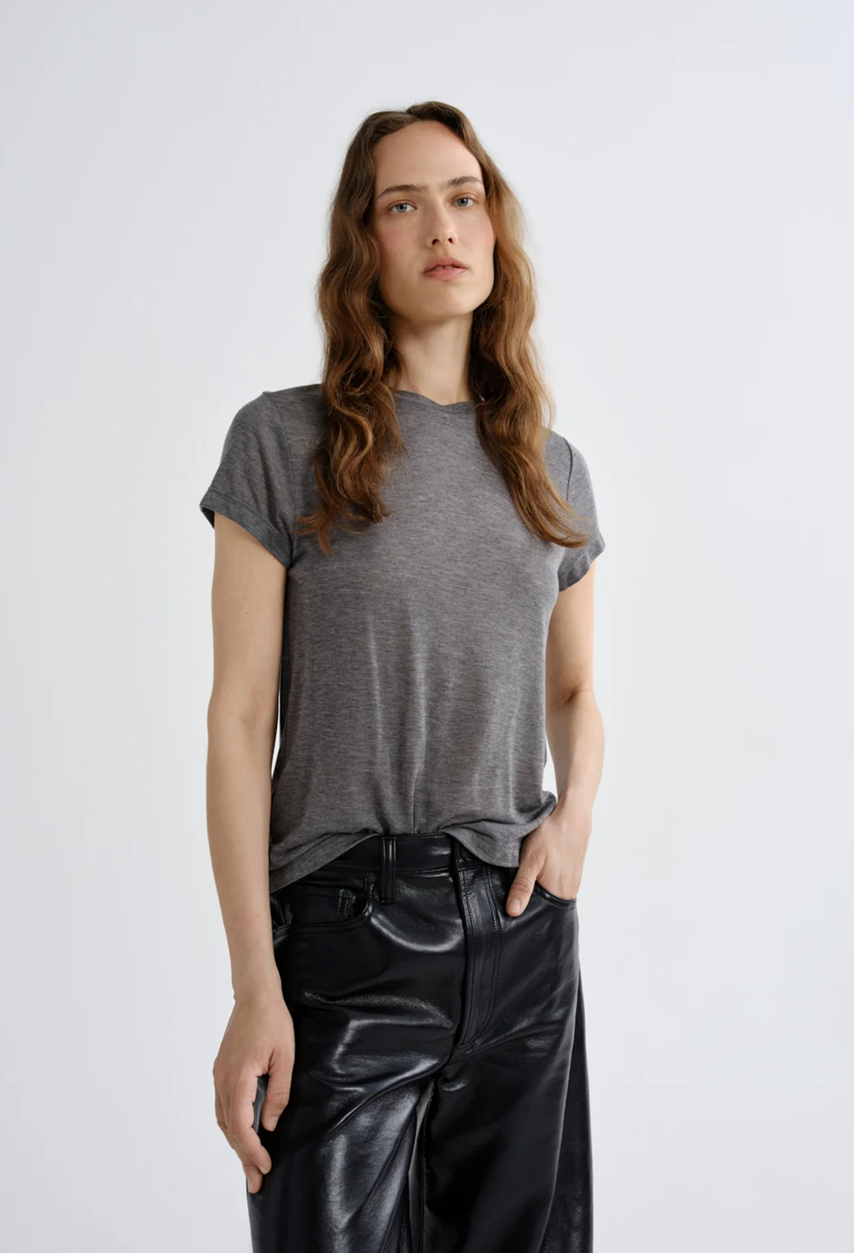 A woman modeling a short-sleeve heather gray t-shirt paired with black wide-leg faux leather pants, shot against a plain light gray studio background.