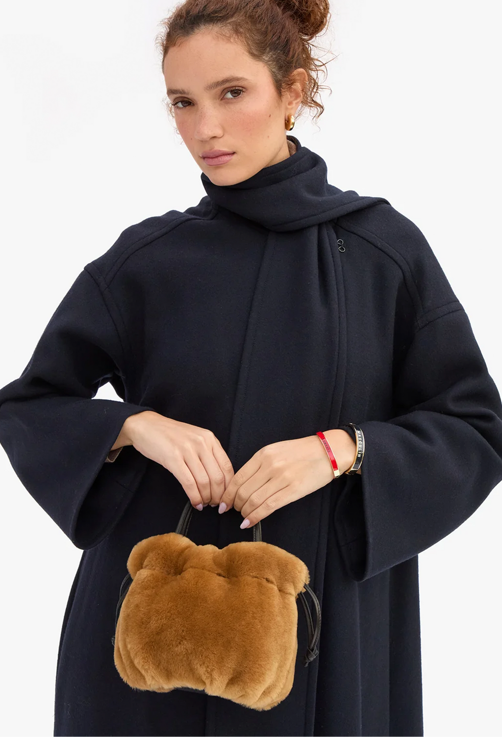 A model wearing a dark navy blue hooded coat holds a small, plush brown teddy bear-shaped handbag against a clean white background.