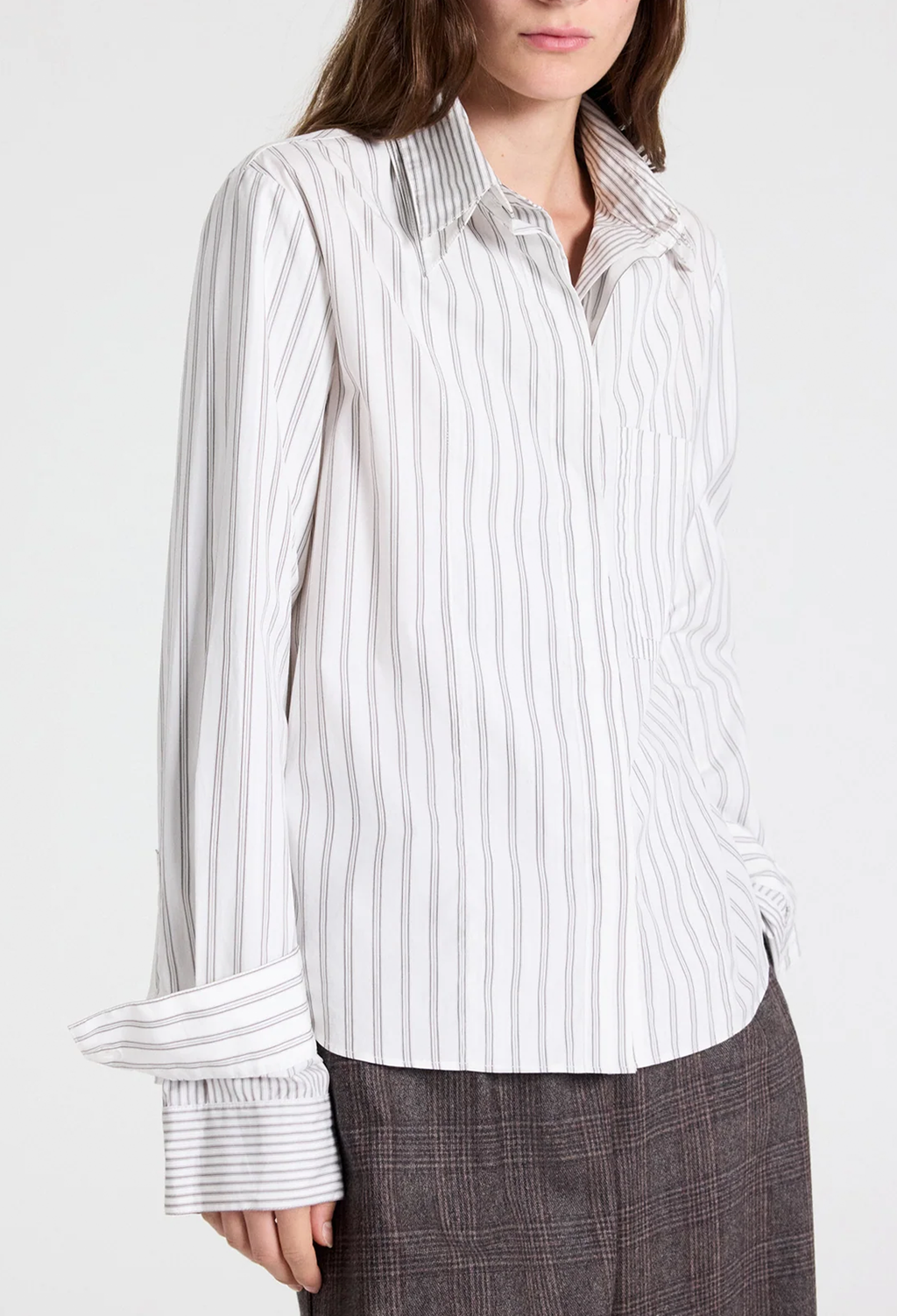 A woman wearing a white button-up shirt with thin vertical gray stripes and dark gray plaid trousers, shown from the neck down against a plain light background.