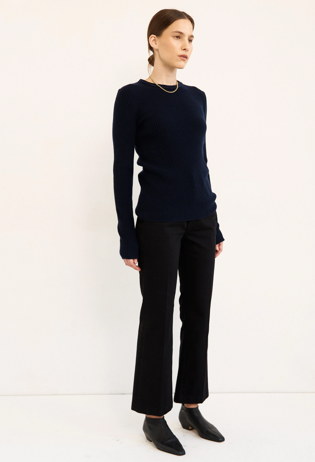 A woman modeling a dark navy blue long-sleeve knit sweater and black wide-leg trousers against a plain white studio background.