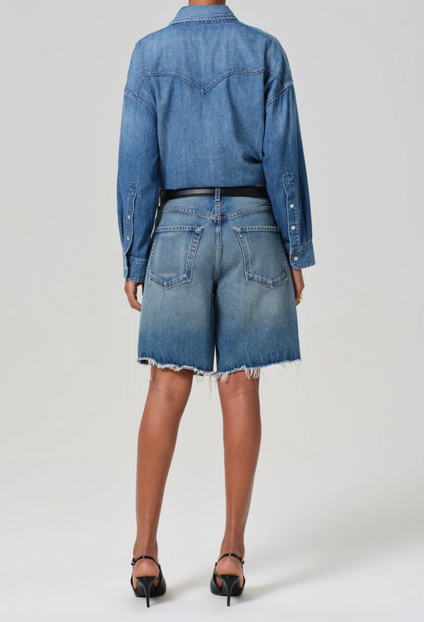 The back of a woman wearing blue denim shorts and a jean jacket. white background