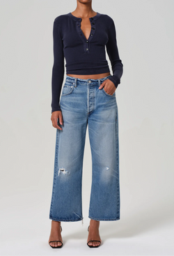 A woman wearing a blue top and wide leg blue jeans with two small rips. white background.