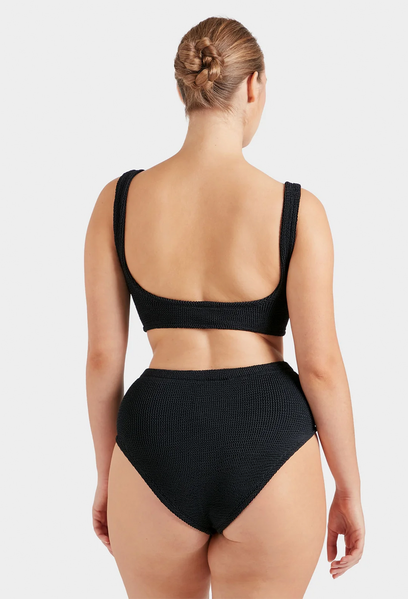 The back of a woman wearing a black two-piece swimsuit with high waisted bottoms. White background.