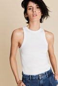 A woman wearing a white ribbed tank top and jeans. Beige background.