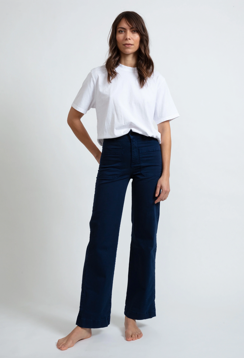 A woman wearing a white tee shirt and dark blue pants with large front pockets. White background.