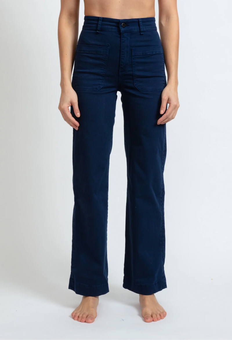 A woman wearing dark blue pants with large front pockets. White background.