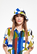 A woman wearing a blue, green, and white bucket hat with a matching dress. White background.