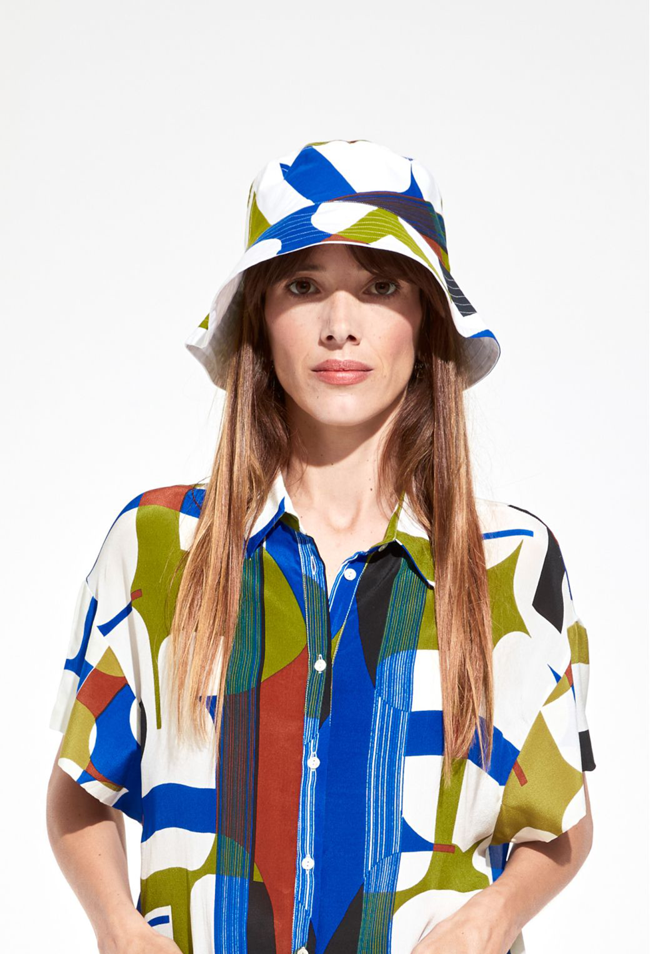 A woman wearing a blue, green, and white bucket hat with a matching dress. White background.