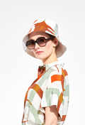 A woman in sunglasses wearing a brown, teal, and white bucket hat with a matching dress. White background.