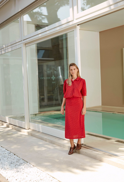 A woman outside of a store wearing a half sleeve red button down shirt with pink polka dots and a shirt pocket and matching long skirt.