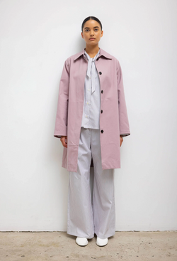 A woman wearing a blue and white striped shirt and pants set with a pink overcoat. White background.