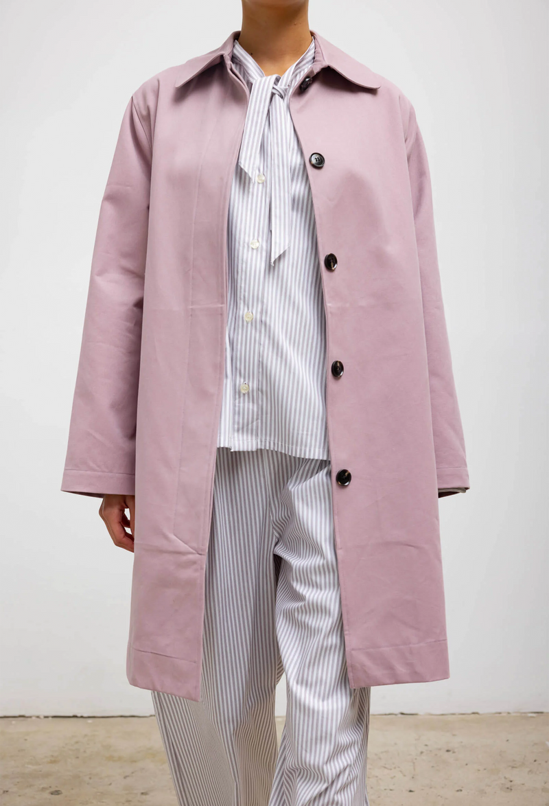 A woman wearing a blue and white striped shirt and pants set with a pink overcoat. White background.