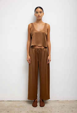 A woman wearing a loose brown tank top and matching pants. White background.
